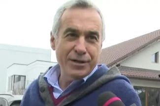 Știri de azi | Avocații lui Călin Georgescu, INTERZIS la dosarele acestuia! Apărătorii candidatului plasat pe primul loc după primul tur al prezidențialelor NU știu nici până acum pe ce probe se bazează procurorii - Știri de azi | Călin Georgescu vorbind cu reporterii în exterior, purtând un gilet gri și o cămașă albastră, cu o expresie preocupată pe față