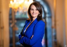 Anca Alexandrescu într-un portret oficial, purtând un sacou albastru, zâmbitoare, pe un fundal elegant