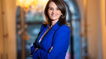 Anca Alexandrescu într-un portret oficial, purtând un sacou albastru, zâmbitoare, pe un fundal elegant