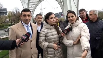 Anca Alexandrescu și George Simion la stația de tramvai Eroii Revoluției, criticând investiția de 5,3 milioane de euro într-o structură decorativă, în timp ce bucureștenii așteaptă tramvaiul în frig și ploaie.